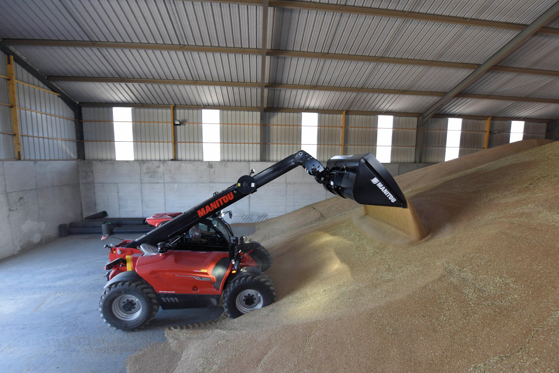 Telehandler Manitou moviendo grano con cuchara dentro de una bodega